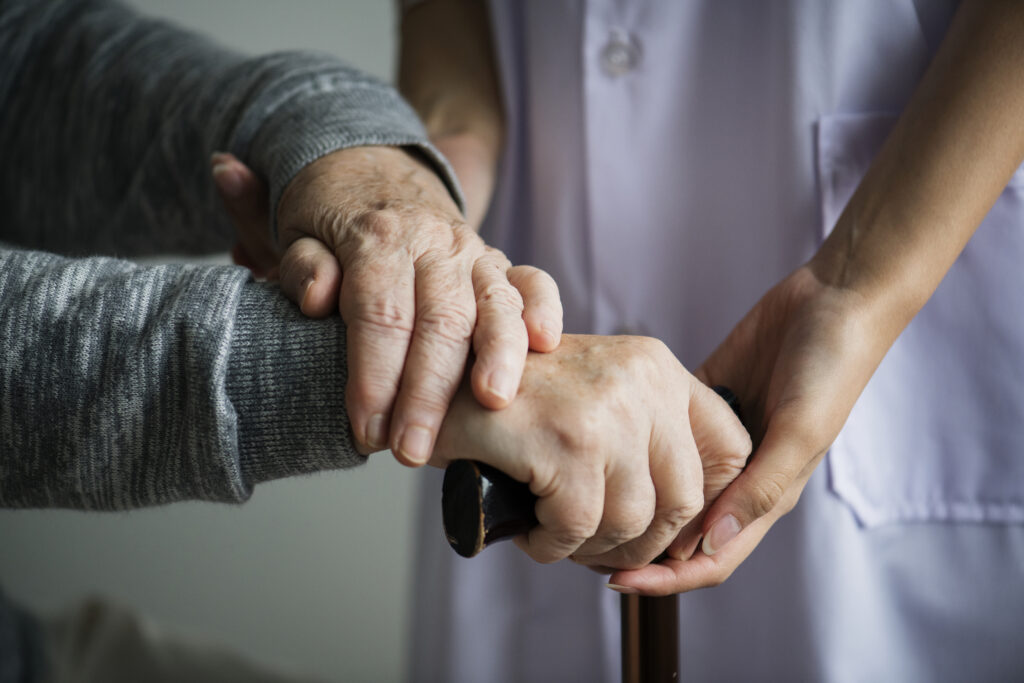 Elderly hand on walking stick supported by a nurse, symbolizing caregiver assistance for elderly in Dubai